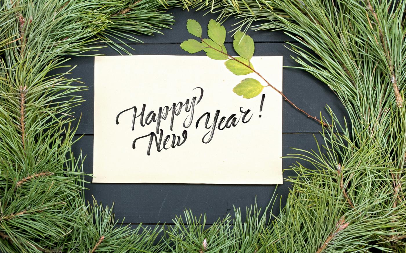 a happy new year's card on top of a pine tree by Kostiantyn Li courtesy of Unsplash.